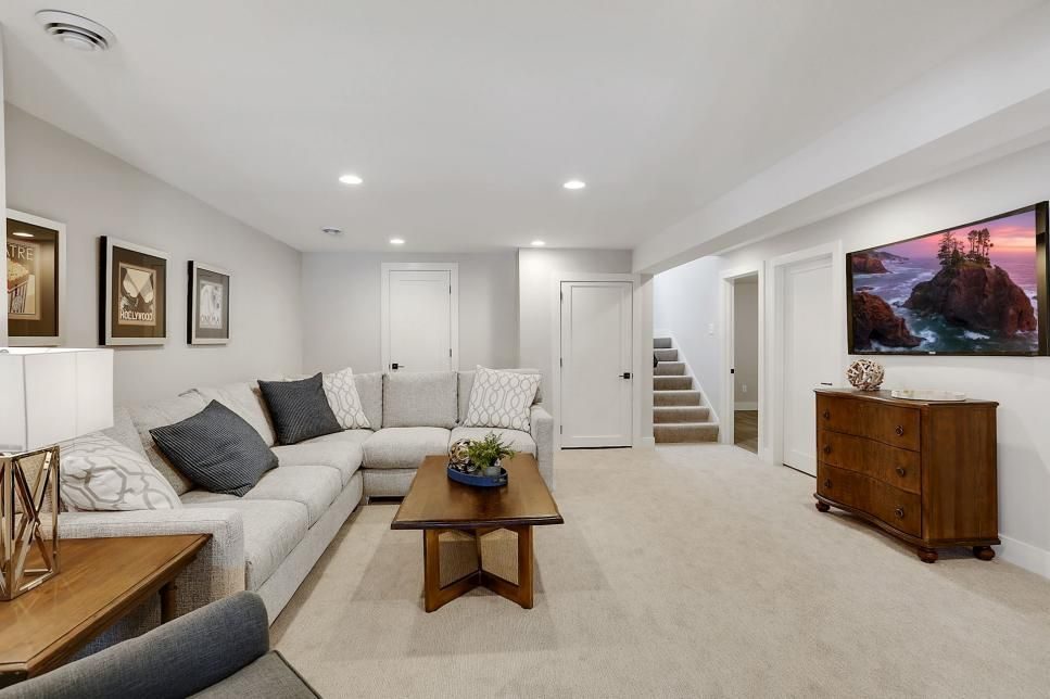 Bright finished basement living area with grey sectional, wood coffee table and artwork